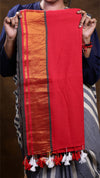 Red and orange fabric with tassels held by a person against a brown background