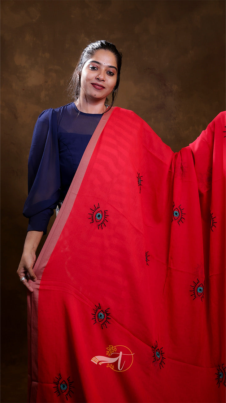 Woman wearing a red saree with black patterns against a brown background