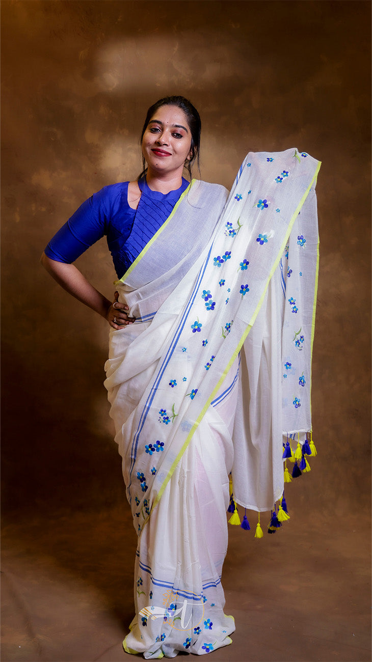 Woman wearing a white saree with blue floral patterns on a brown background