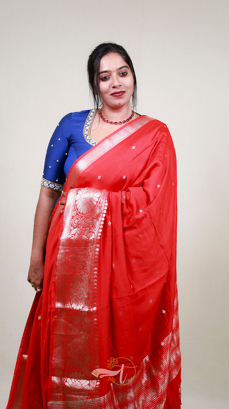 Woman wearing a red saree with a blue blouse against a plain background