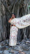 Woman in a floral saree standing in front of a large tree with intricate roots.