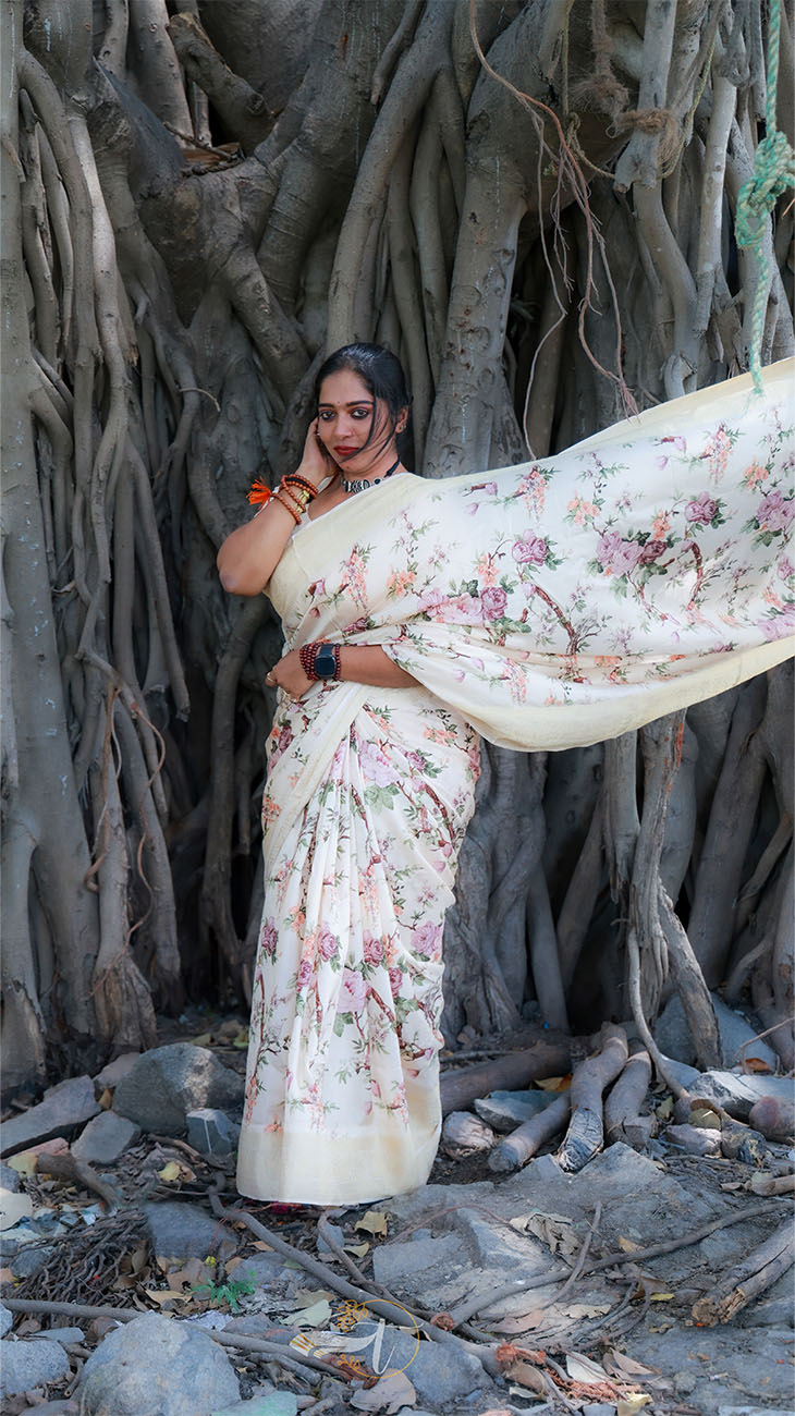 Woman in a floral saree standing in front of a large tree with intricate roots.