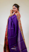 Woman wearing a purple saree with a colorful border against a white background