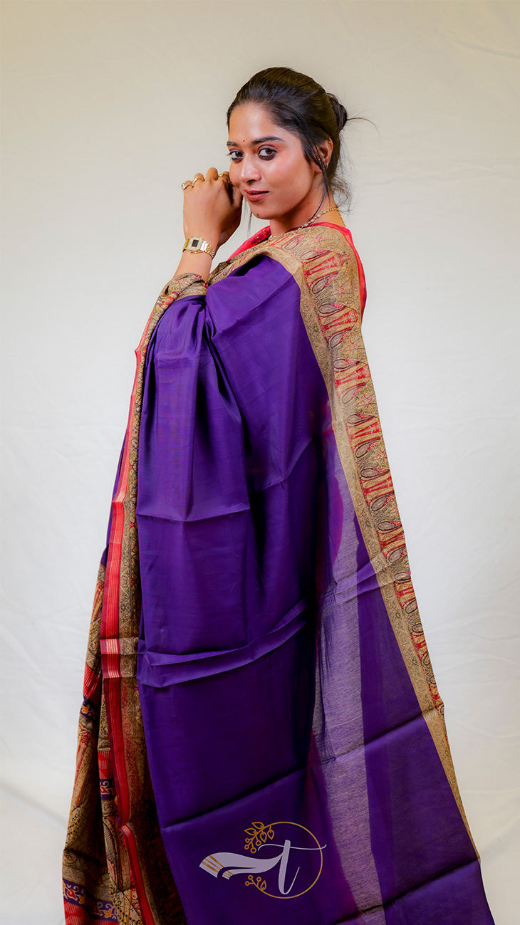 Woman wearing a purple saree with a colorful border against a white background