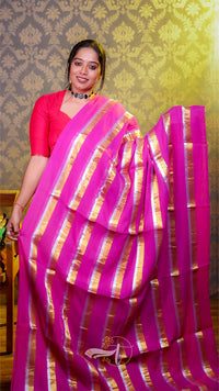Woman wearing a pink saree with gold stripes against a patterned wall.