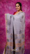 Woman wearing a light purple saree with black patterns against a pink background