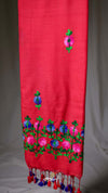 Red fabric with floral embroidery and tassels on a gray background