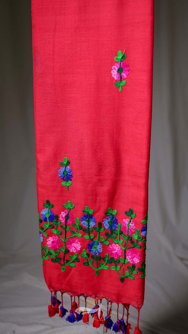 Red fabric with floral embroidery and tassels on a gray background