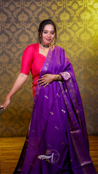 Woman wearing a purple saree with a red blouse against a patterned wall.