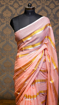 Pink saree with gold stripes on a mannequin against a patterned wall.