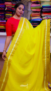 Woman wearing a yellow saree with a red blouse in front of fabric stacks.