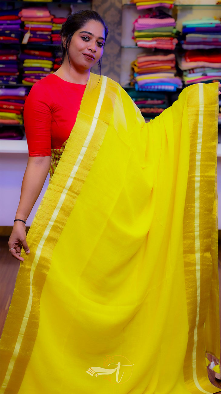 Woman wearing a yellow saree with a red blouse in front of fabric stacks.