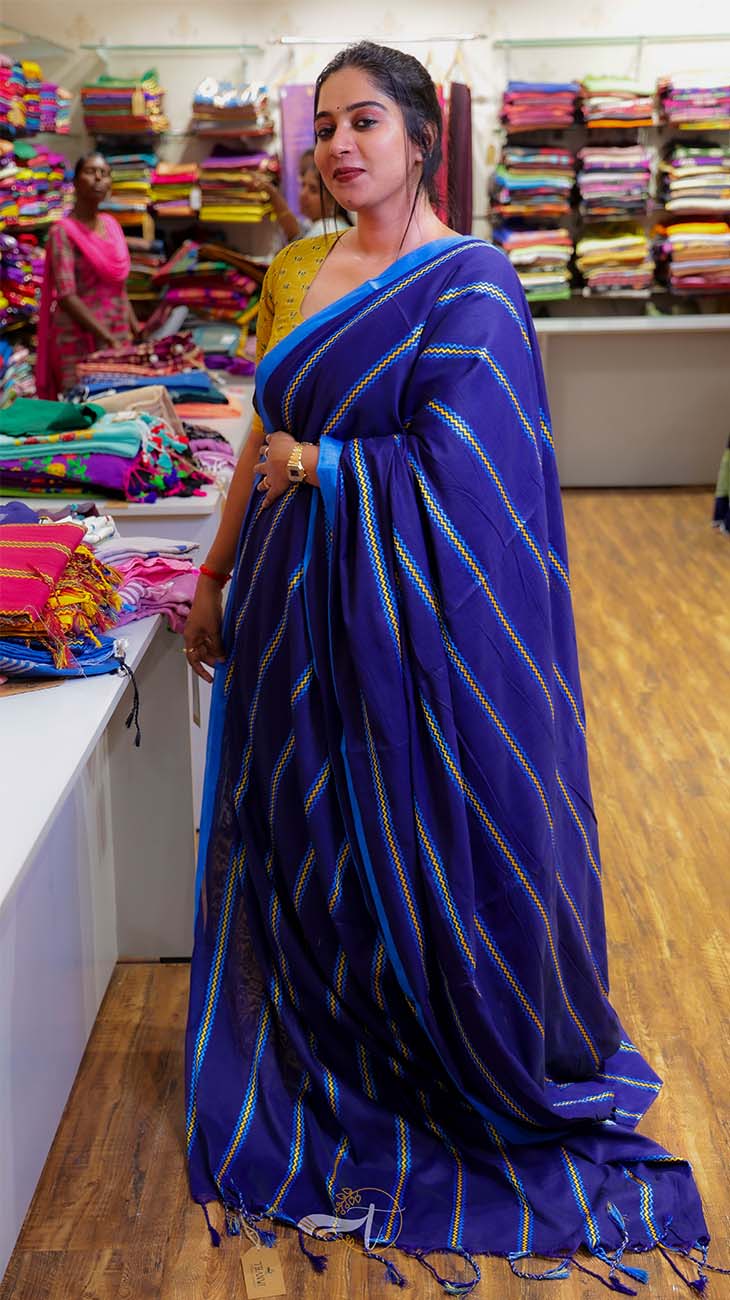Woman wearing a blue saree with a striped pattern in a fabric store.