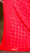 Red fabric with white grid pattern held by a hand against a brown background