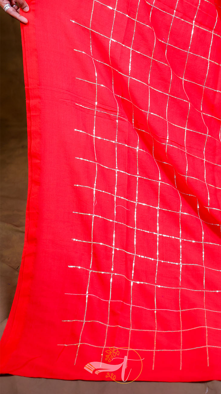Red fabric with white grid pattern held by a hand against a brown background