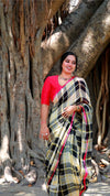 Woman in a colorful saree standing in front of a large tree with intricate root system.