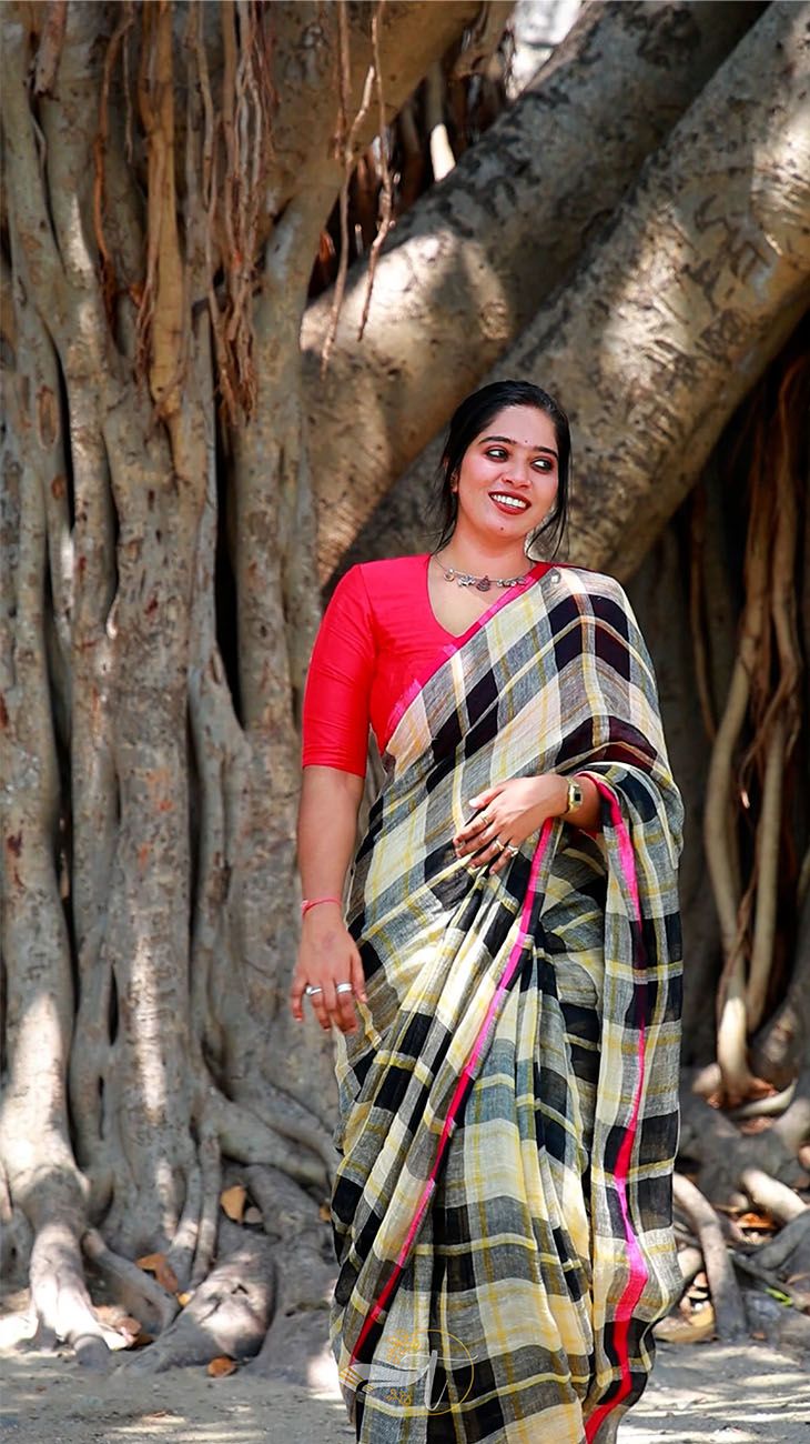 Woman in a colorful saree standing in front of a large tree with intricate root system.