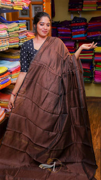 Woman holding a brown saree in a fabric store with colorful fabrics in the background