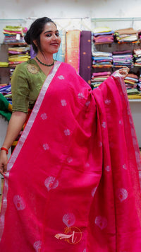 Woman holding a pink saree with a visible brand logo in a fabric store.