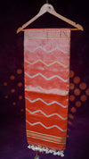 Orange fabric with white wave patterns hanging on a wooden hanger against a dark background