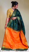 Woman wearing a green and orange saree with a plain background