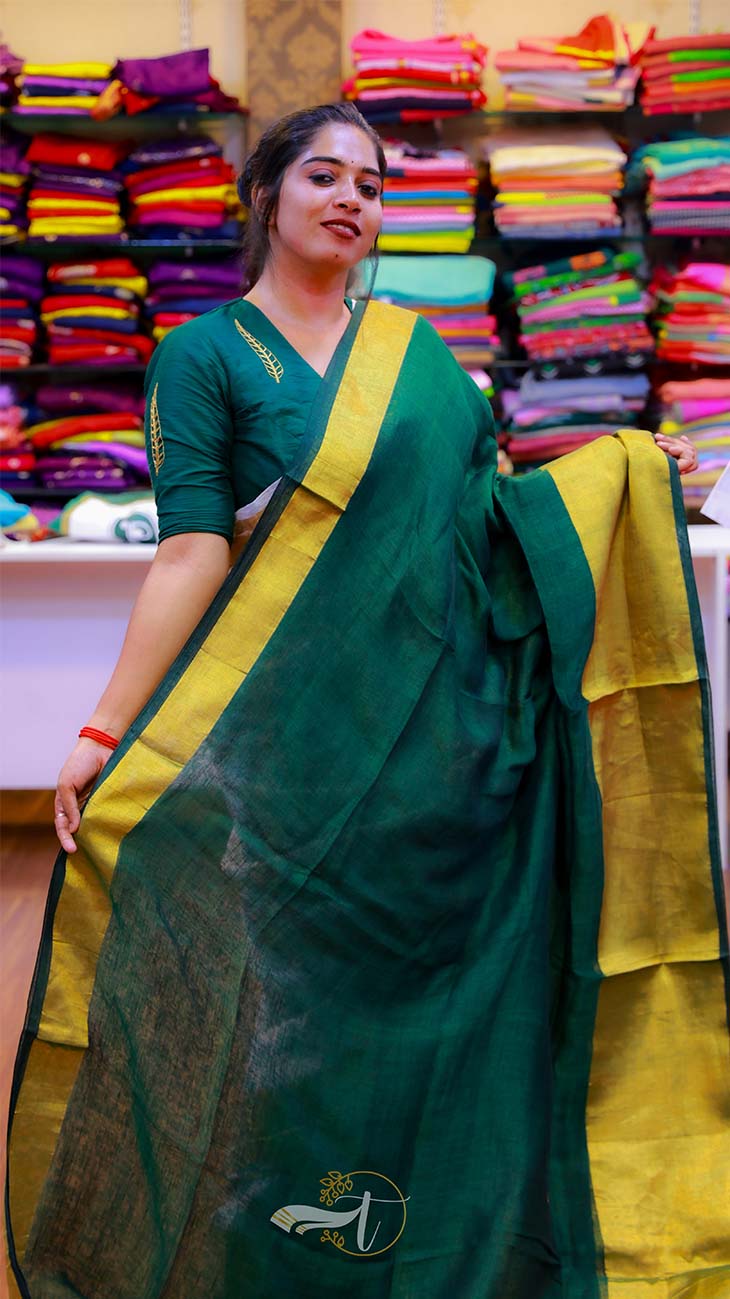 Woman wearing a green saree with yellow border in front of colorful fabric displays.