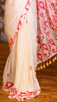 White saree with red patterns and yellow tassels on a wooden floor