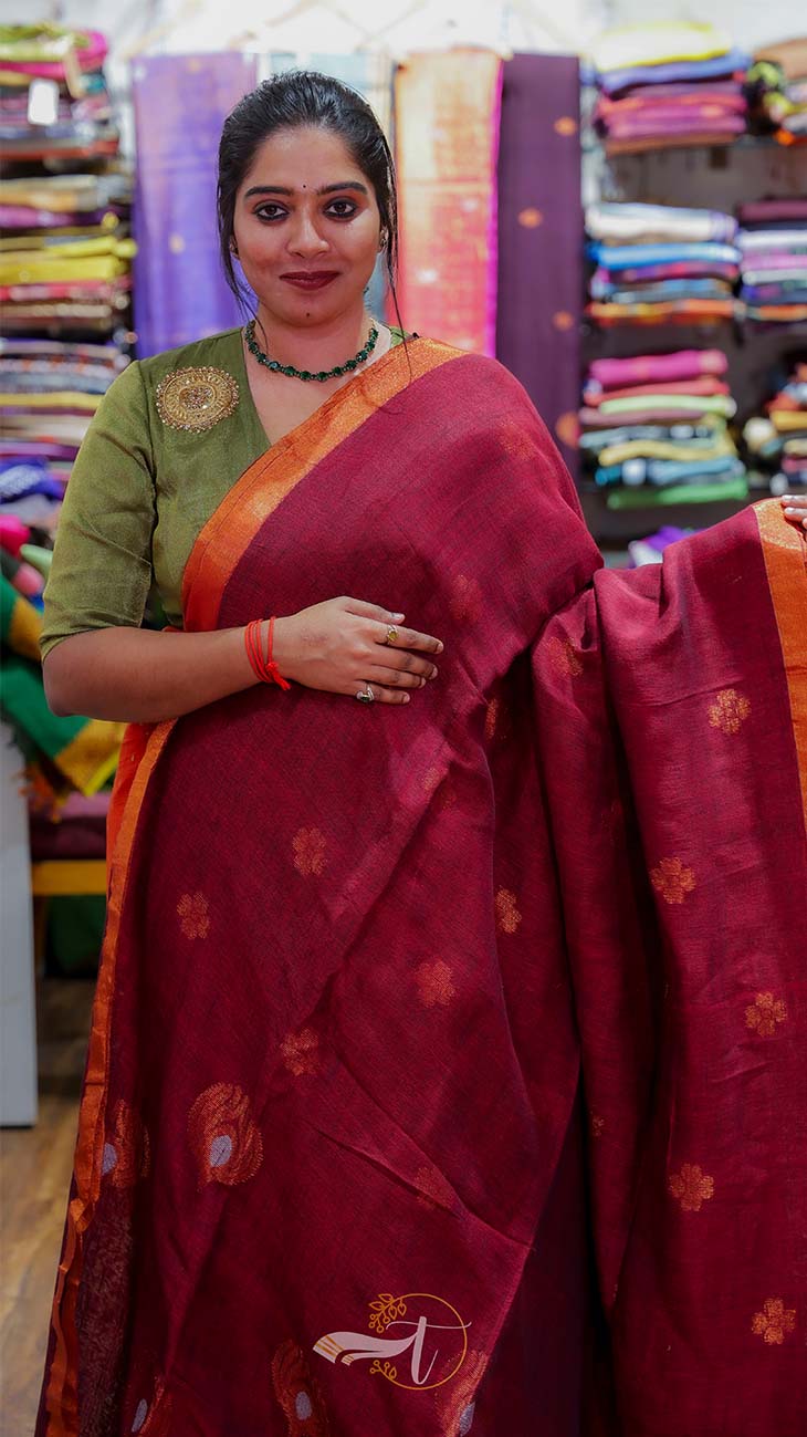 Woman wearing a maroon saree with a green blouse in a fabric store.