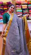 Woman holding a gray saree with a gold border in a fabric store.