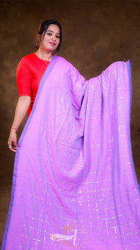 Woman wearing a bright purple saree with a red blouse against a brown background