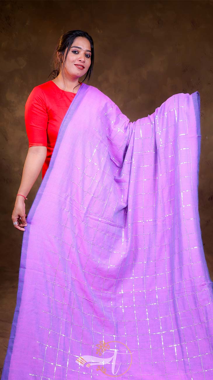 Woman wearing a bright purple saree with a red blouse against a brown background