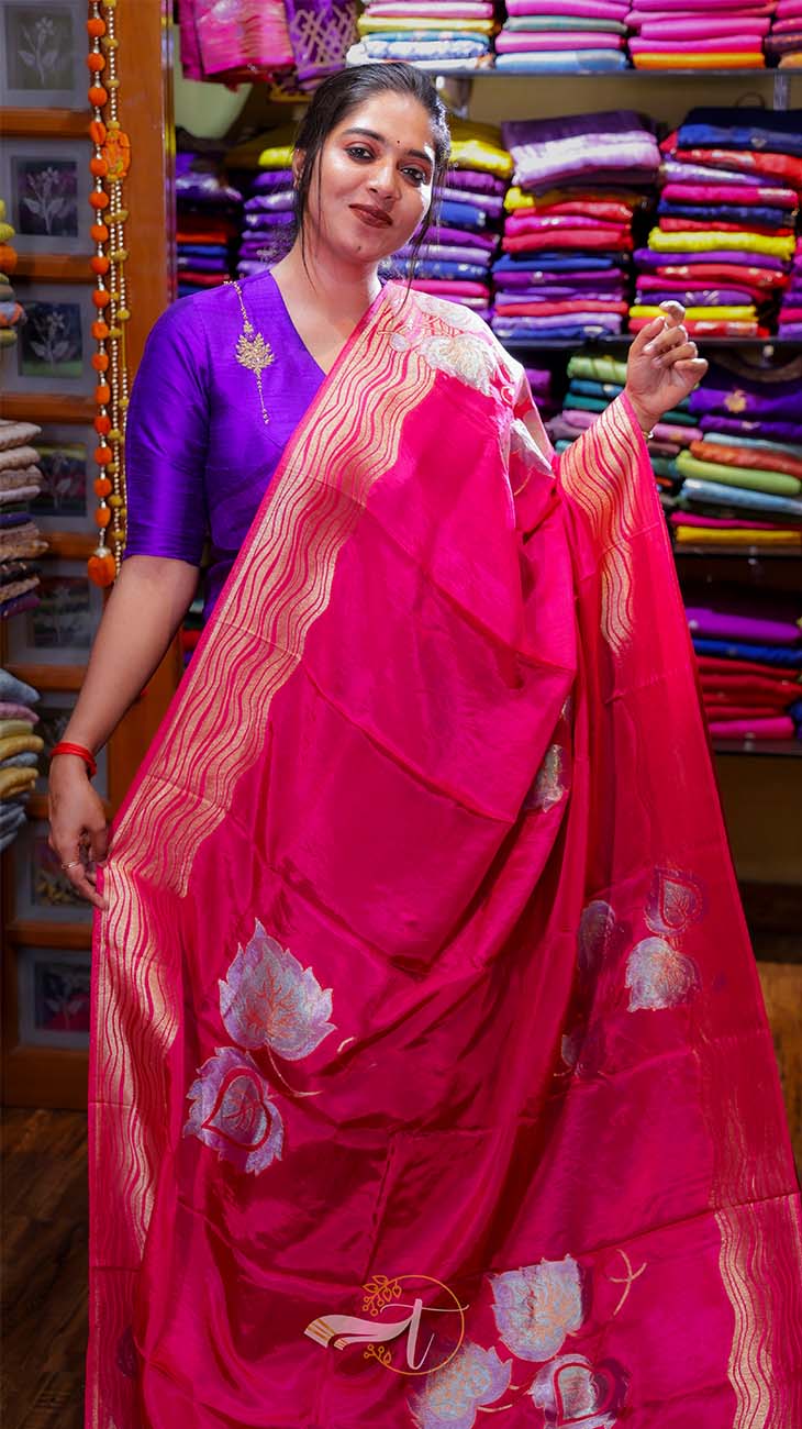Woman wearing a bright pink saree with floral patterns in a fabric store.