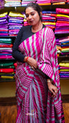Woman wearing a pink and gray striped saree in front of colorful fabric background