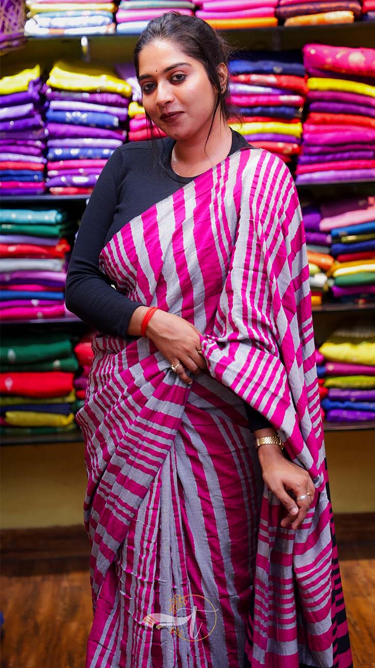 Woman wearing a pink and gray striped saree in front of colorful fabric background