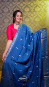 Woman wearing a blue saree with a pink blouse against a decorative green and gold background