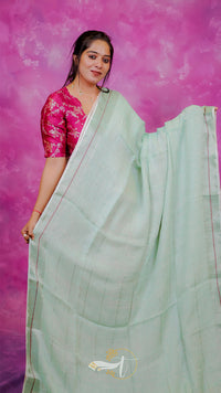 Woman wearing a light green saree with a pink blouse against a pink background