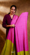 Woman holding a pink and green saree against a brown background
