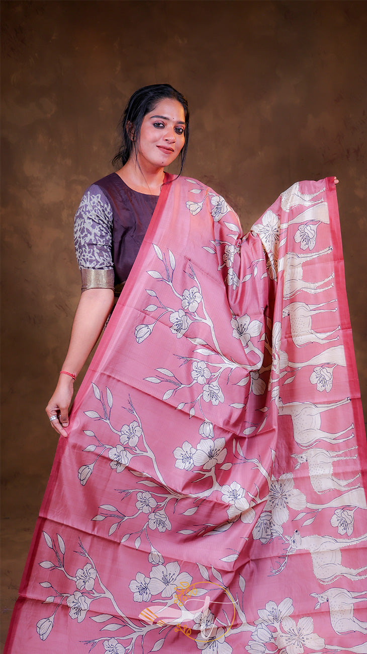 Woman wearing a pink saree with floral patterns against a brown background