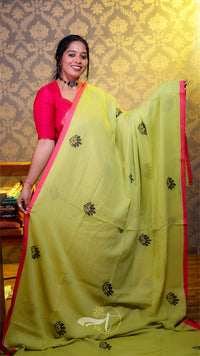 Woman wearing a light green saree with black patterns and a pink blouse against a decorative wall.