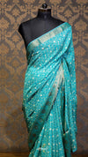 Teal saree with white patterns on a mannequin against a patterned wall.