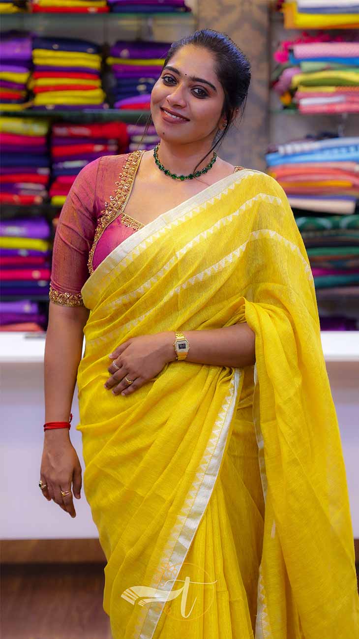 Woman in a yellow saree standing in front of colorful fabric stacks