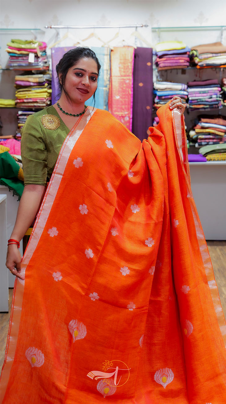 Woman holding an orange saree with a background of fabric racks.