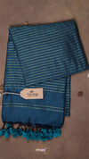 Blue striped towel with tassels on a brown background, featuring a 'THANUKI' tag.