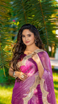 Woman in a purple saree with green foliage in the background