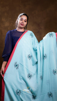 Woman wearing a light blue saree with black patterns against a brown background
