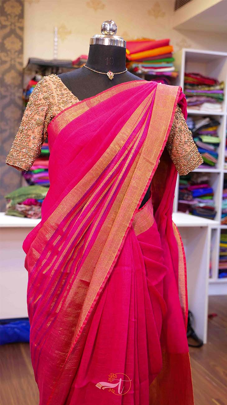 Red saree with gold border on a mannequin against a backdrop of colorful fabrics.