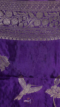 Close-up of a purple fabric with gold embroidery featuring floral patterns and a bird design.