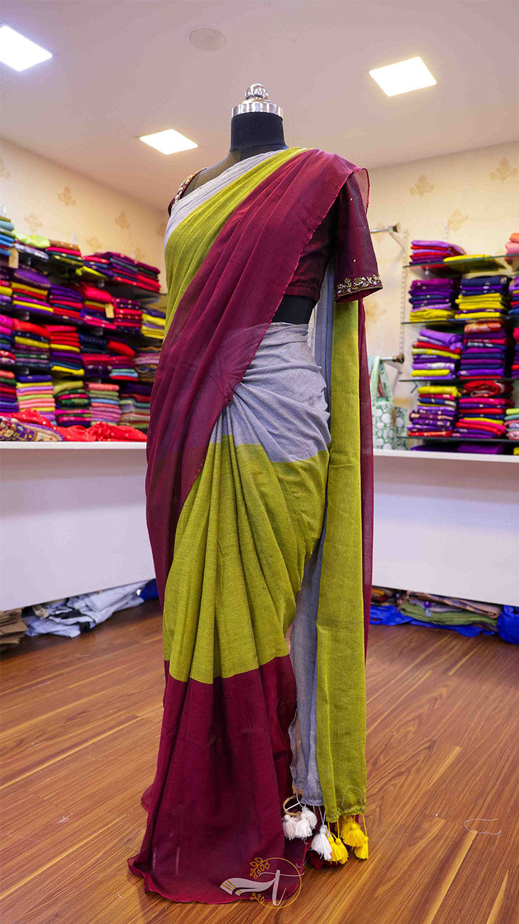 Mannequin wearing a maroon and green saree in a store setting with colorful fabrics in the background.