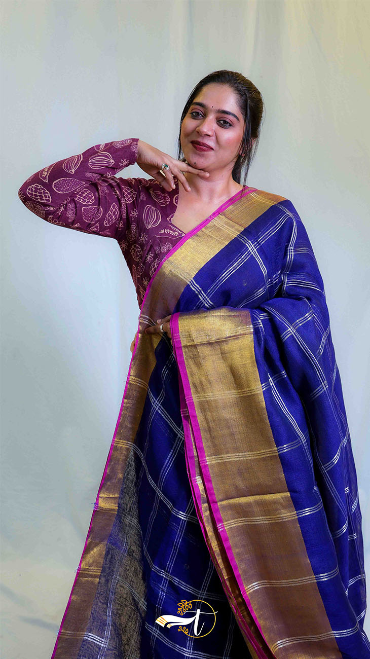 Woman wearing a traditional blue saree with a gold border against a white background
