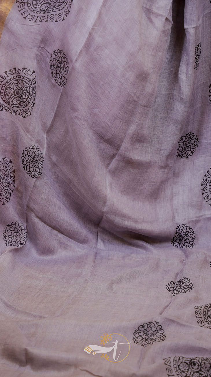 Close-up of a light purple fabric with black floral patterns, brand logo visible.